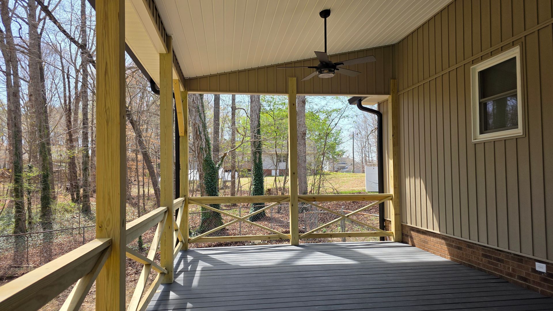 A screened in porch with a ceiling fan and a view of the woods.