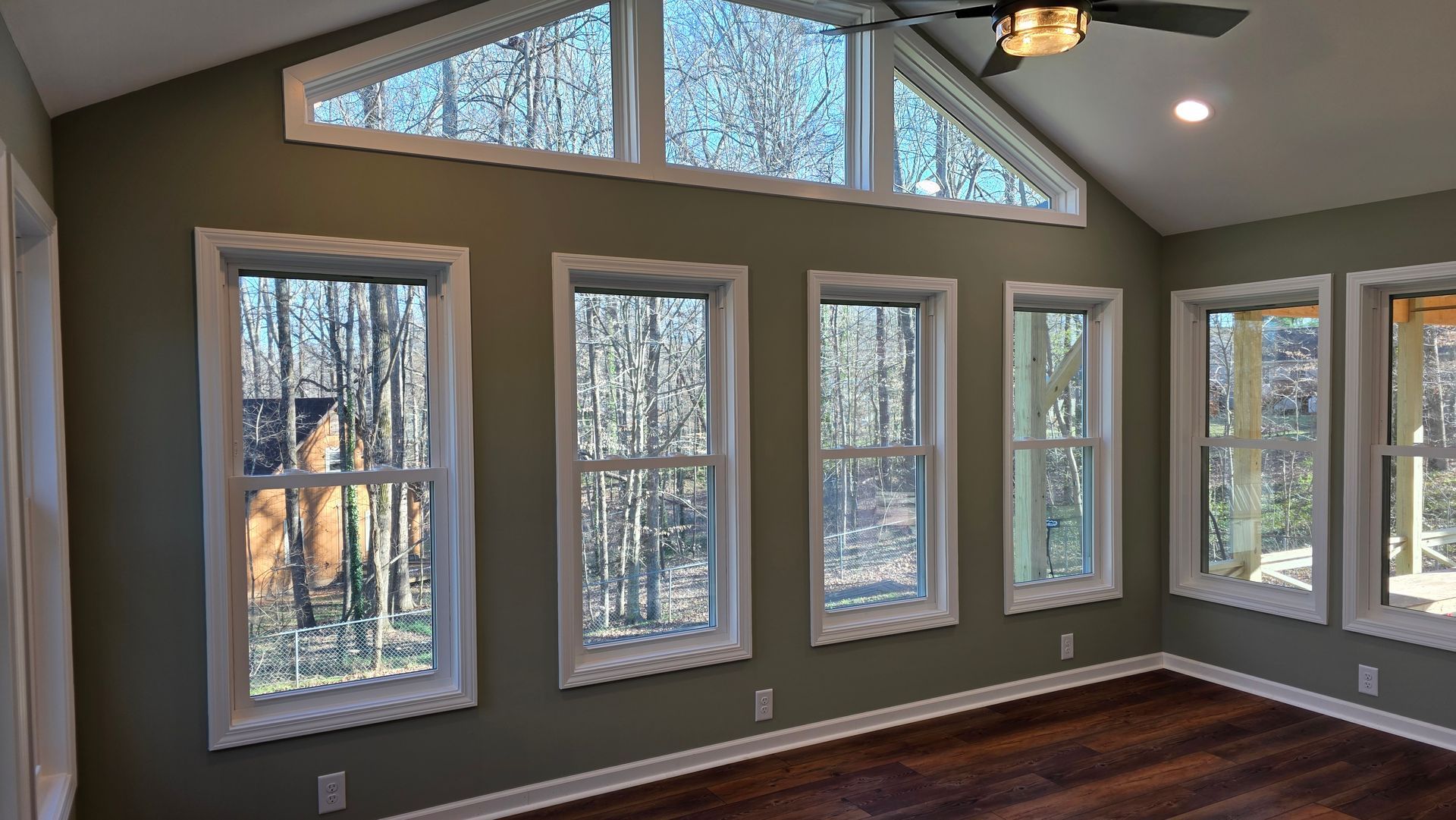 A room with several windows and a slanted ceiling. The walls are olive green and the floors are dark wood.