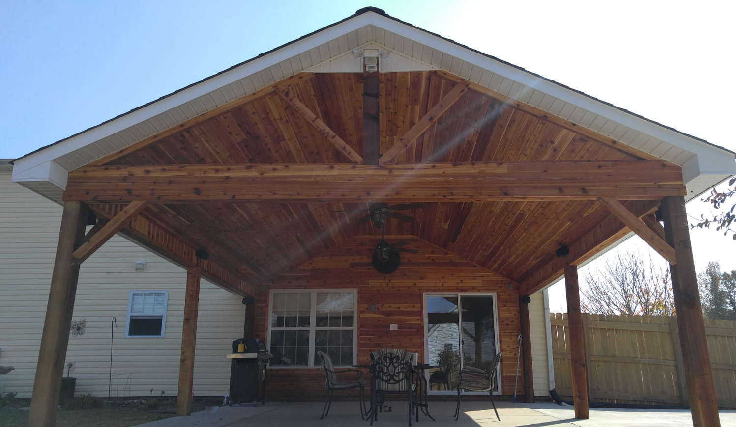 A wooden covered patio area with a table and chairs under a roof.
