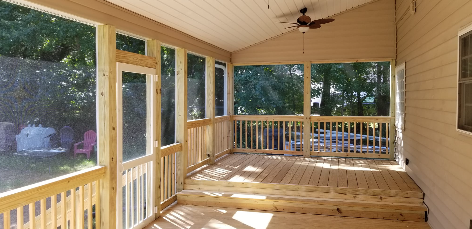 A screened in porch with a wooden deck and a ceiling fan.