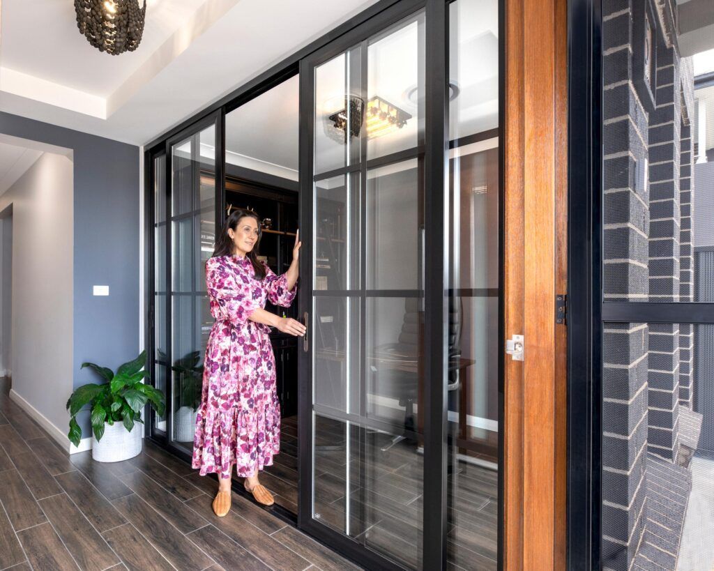 Woman in a pink dress opening black-framed glass sliding doors in a hallway with wood floors.