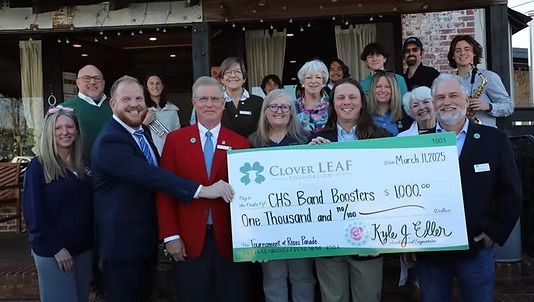 Group presents a large check to CMS Band Boosters. People smile outside a building, holding a large check.