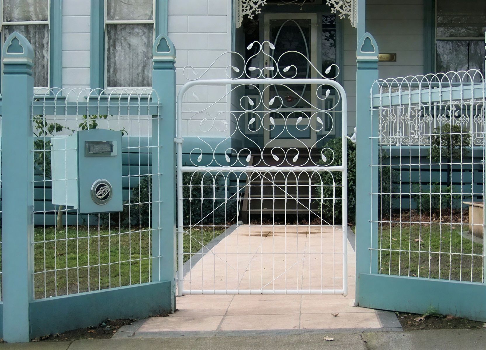 A white gate stands besides a blue fence and a blue door.