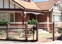 A red brick house surrounded by a fence, featuring a gate at the entrance.