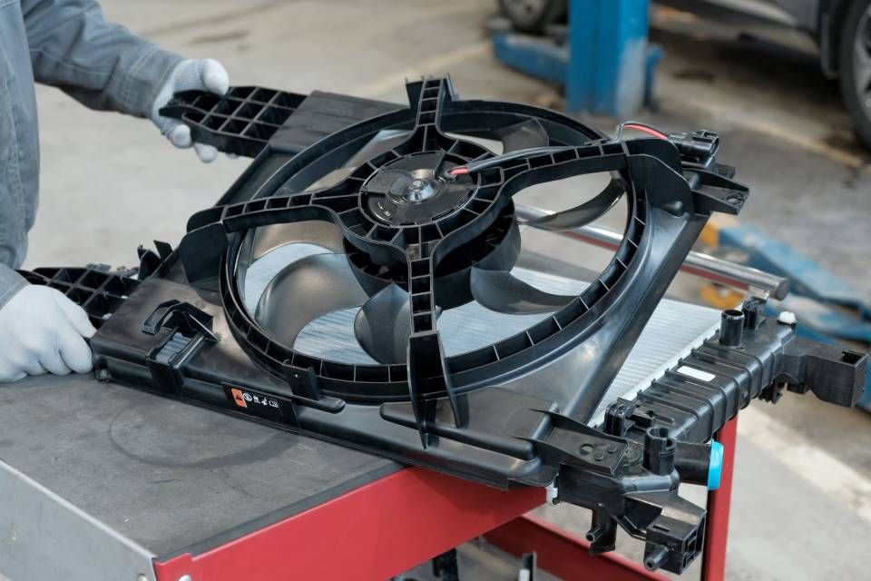 Person holding a car radiator cooling fan assembly in a garage.