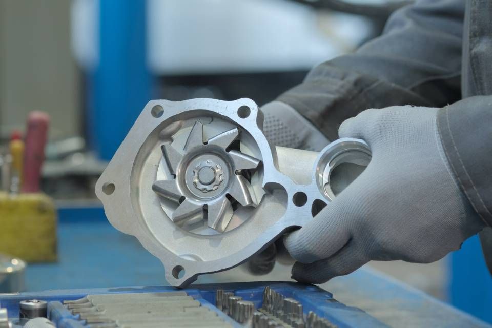 Person wearing gloves holding an open water pump, likely in a workshop setting.