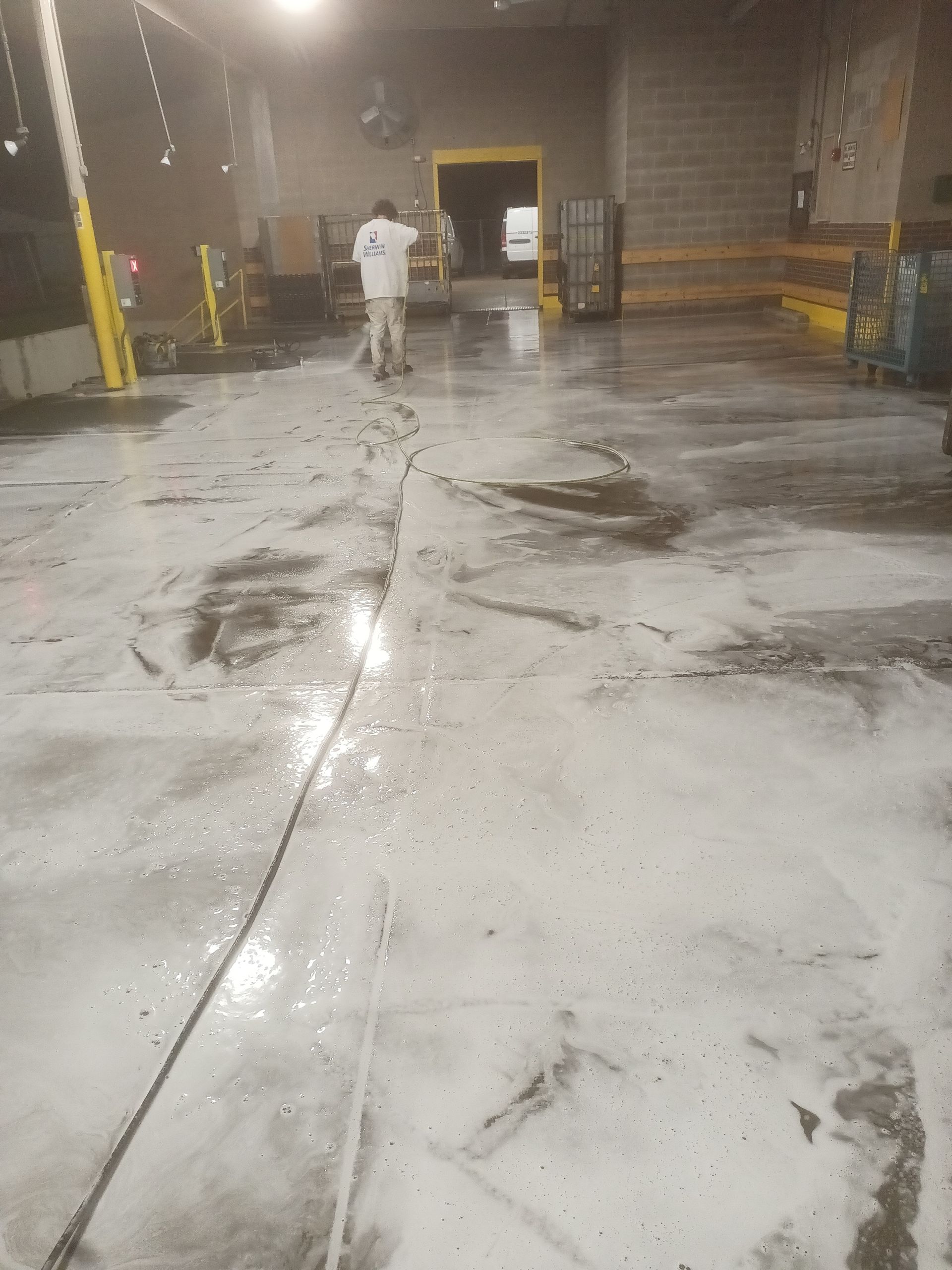 Pressure washing in progress on warehouse floor before applying industrial floor coating
