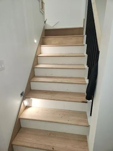 Wooden staircase with white risers and black railing, leading upwards.