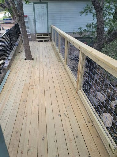 Wooden deck with wire railing, leading to a door and trees.