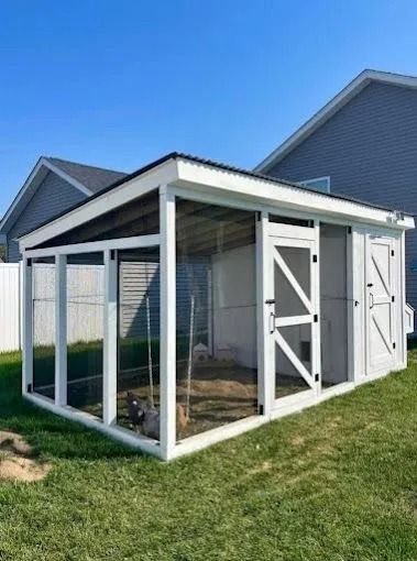 White chicken coop in a grassy backyard with a blue sky.