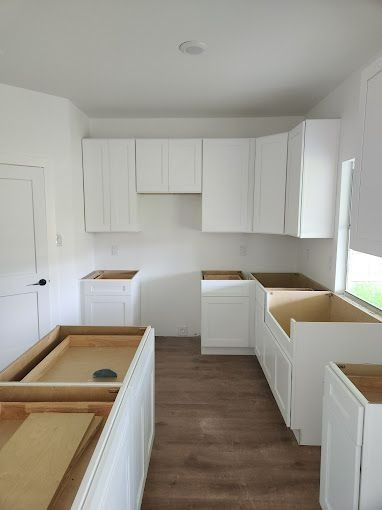 White kitchen cabinets being installed in a room with wood-look flooring and white walls.