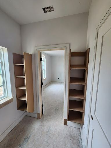 Interior view of a room with unfinished shelves flanking a doorway and a window.