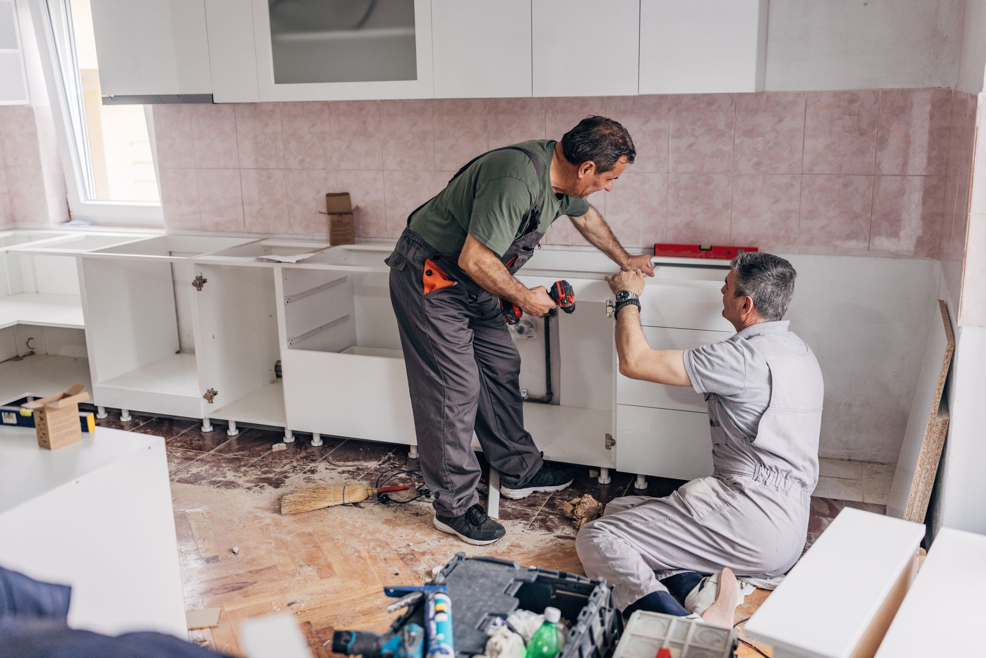 Two workers remodeling a white kitchen.