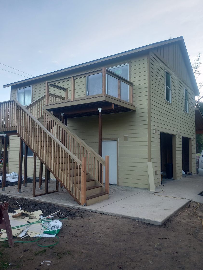 Two-story house under construction with exterior stairs, balcony, and unfinished ground around it