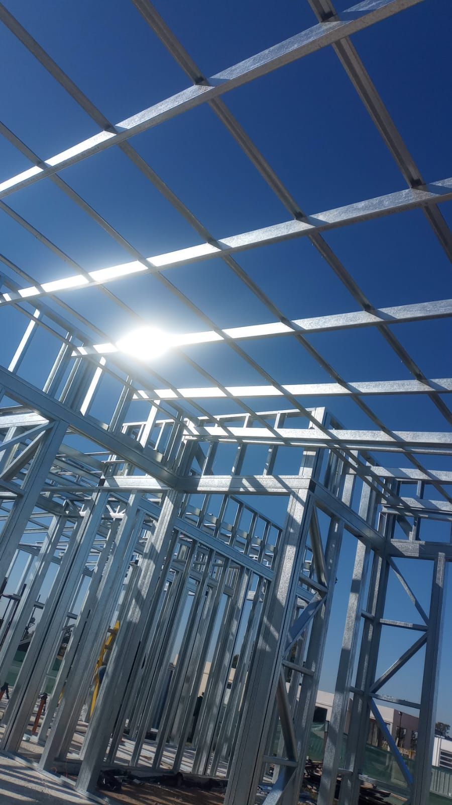 Estructura de acero de un edificio en construcción contra un cielo azul brillante con el resplandor del sol.