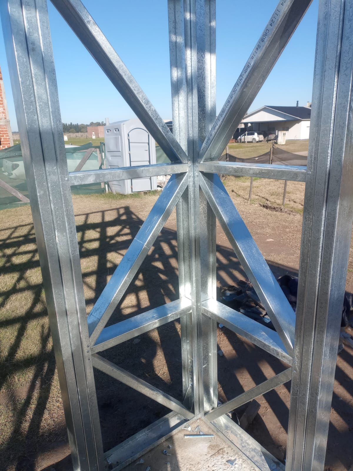 Estructura metálica de torre con refuerzos en forma de X en un campo soleado al aire libre, vista desde el interior de la estructura.