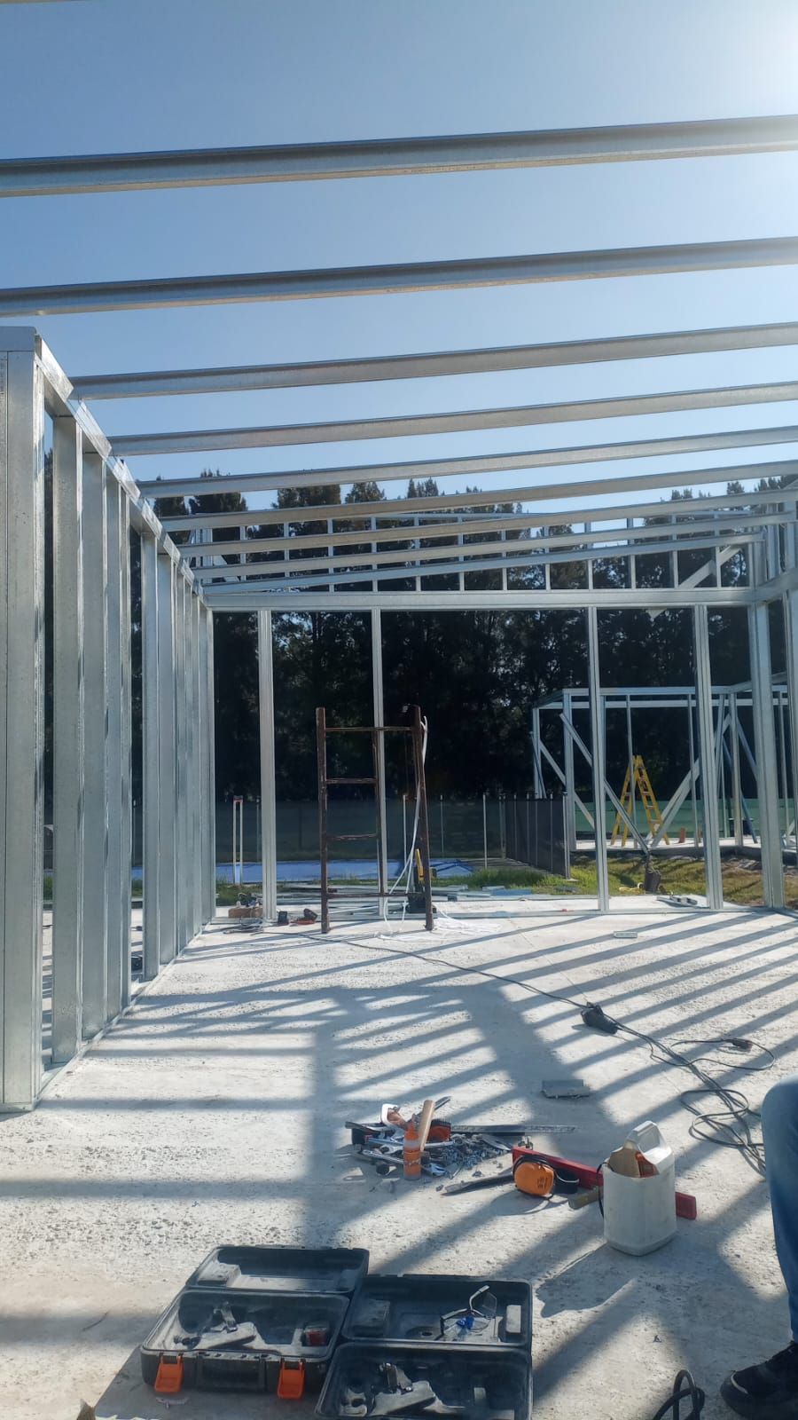 Estructura de una casa parcialmente construida con vigas de acero y herramientas de construcción sobre un piso de concreto bajo un cielo despejado.
