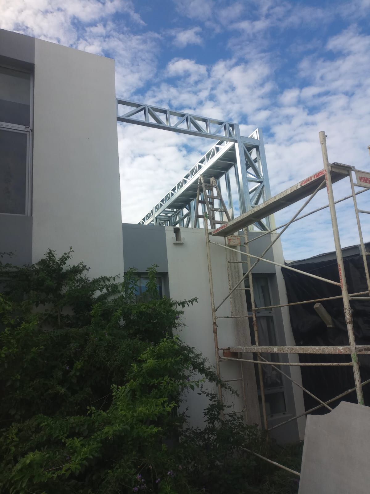 Edificio en construcción con andamios y estructura de acero contra un cielo azul nublado.