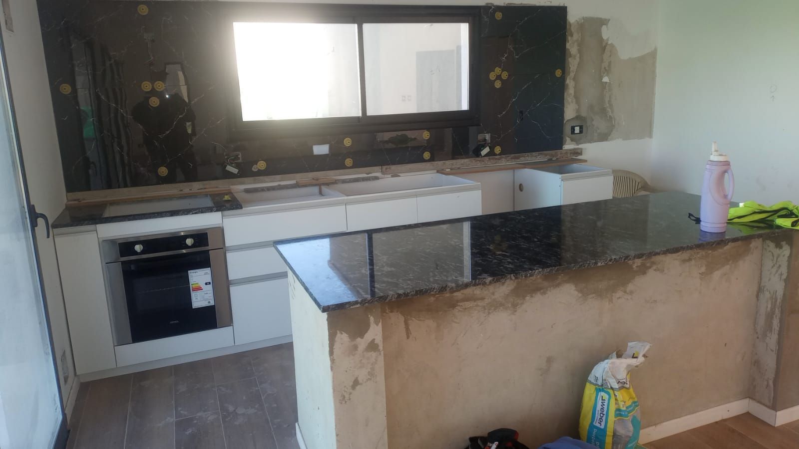 Cocina pequeña con armarios blancos, encimeras oscuras, una isla central y una ventana sobre el fregadero.