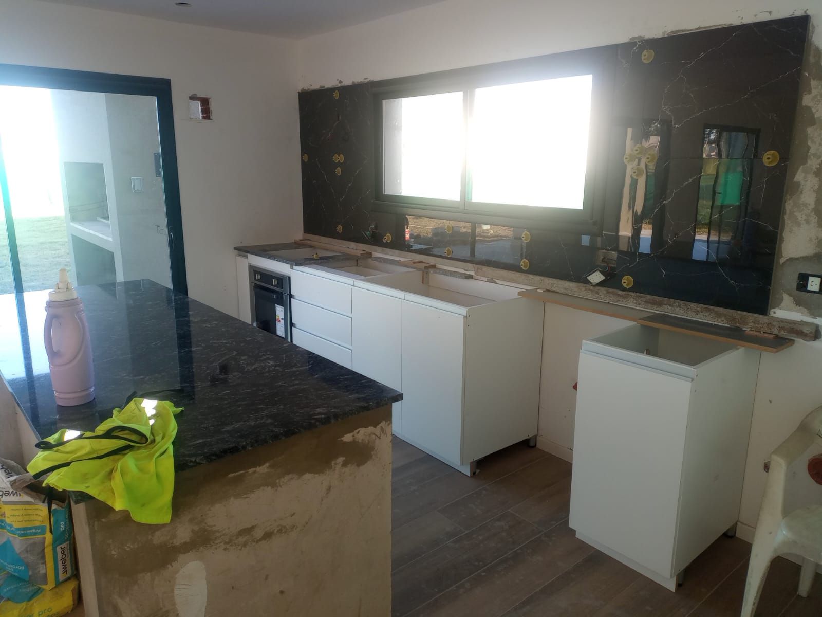 Cocina sin terminar con armarios blancos, encimeras oscuras y una ventana luminosa sobre el fregadero.