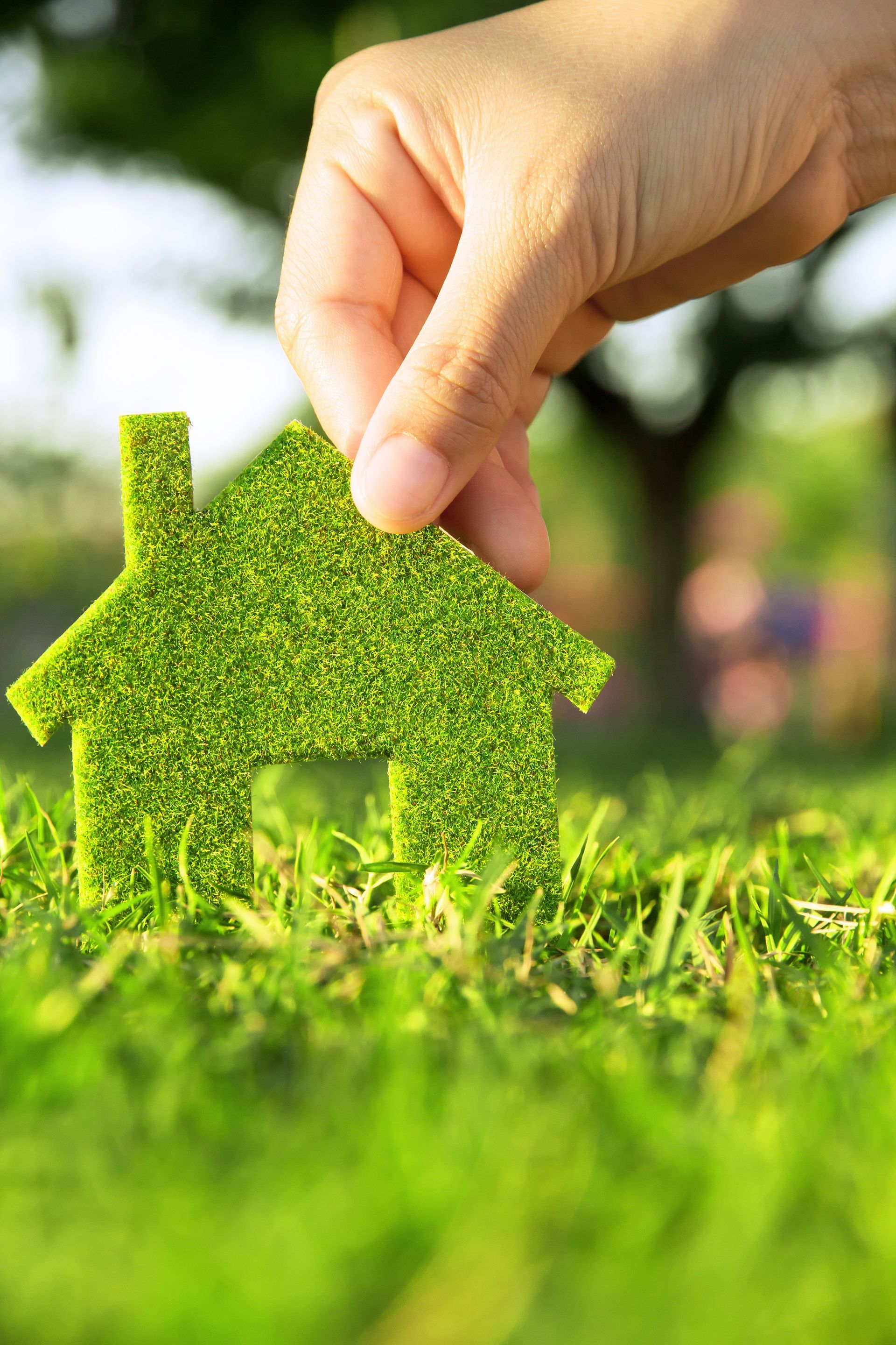 Hand placing a small green house-shaped patch in grass, symbolizing eco-friendly housing