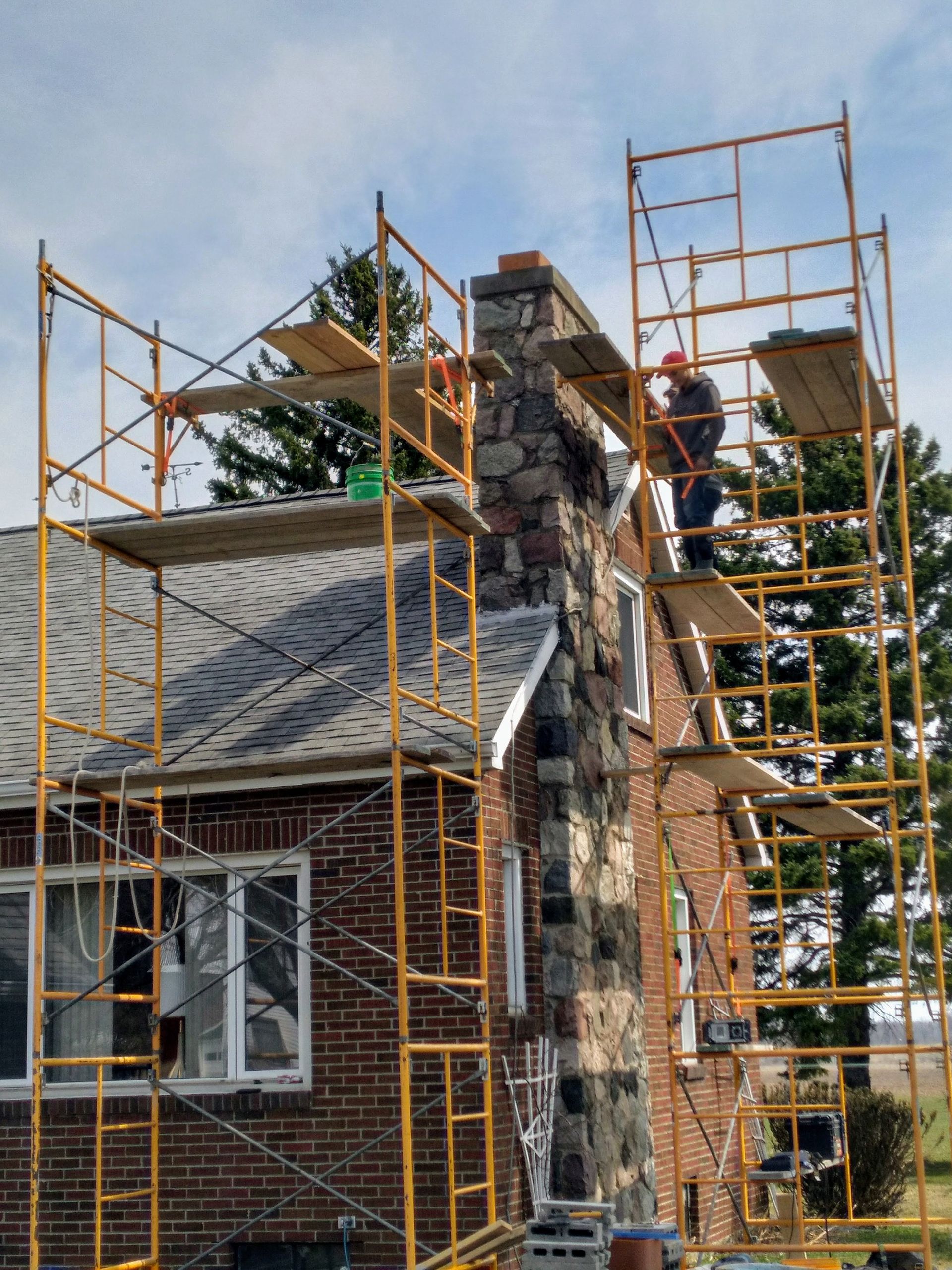 A man is working on a chimney on top of a brick house