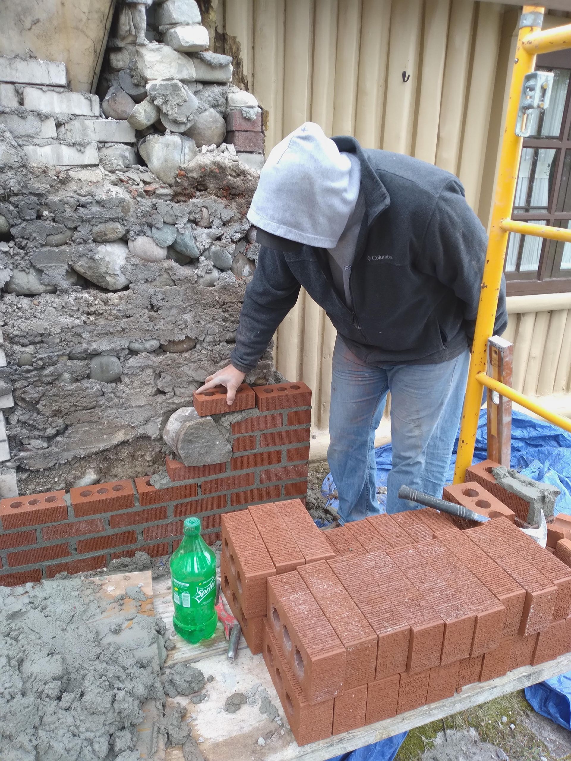 A man is laying bricks on a scaffolding.