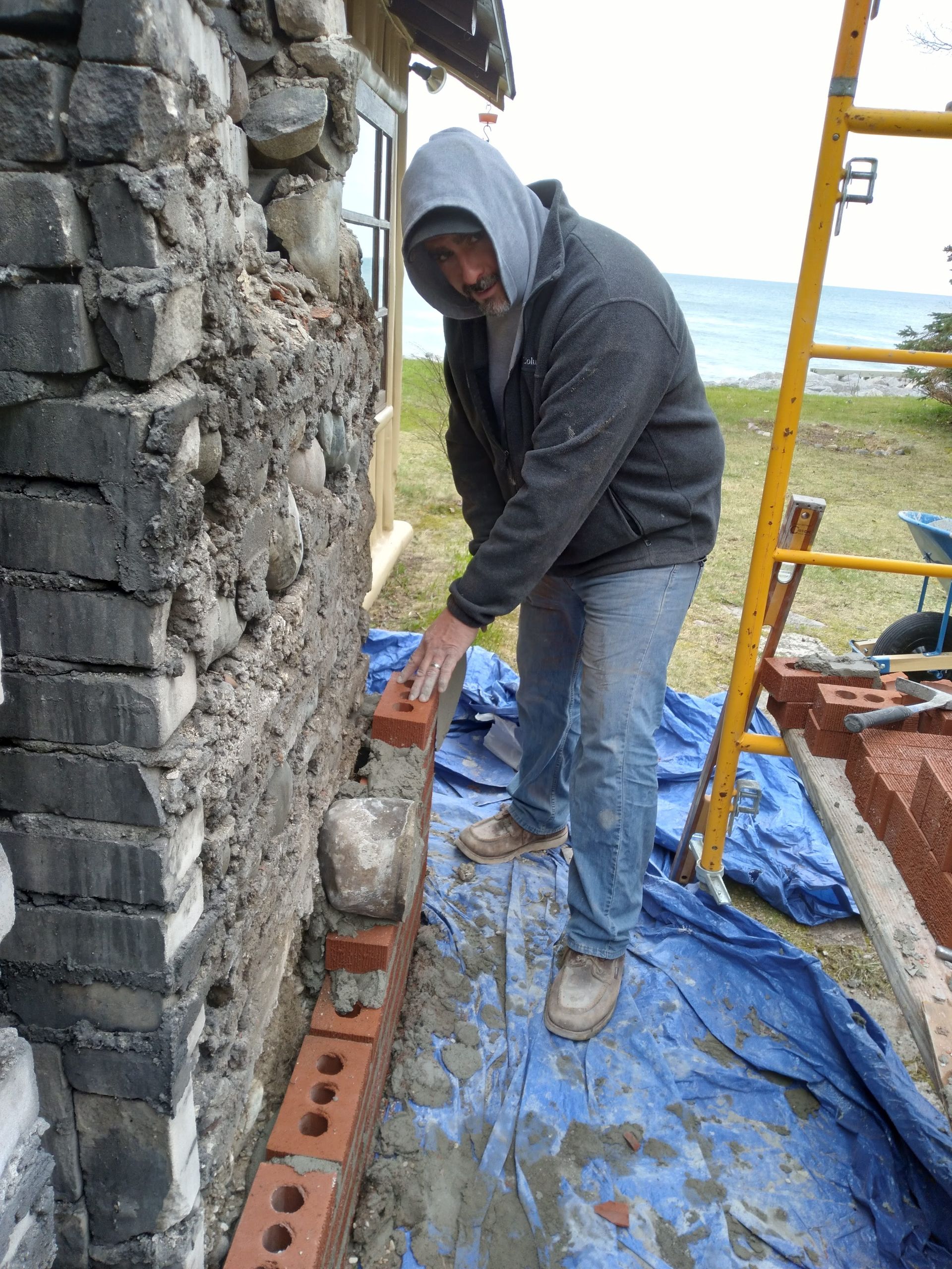 A man is laying bricks on the side of a building