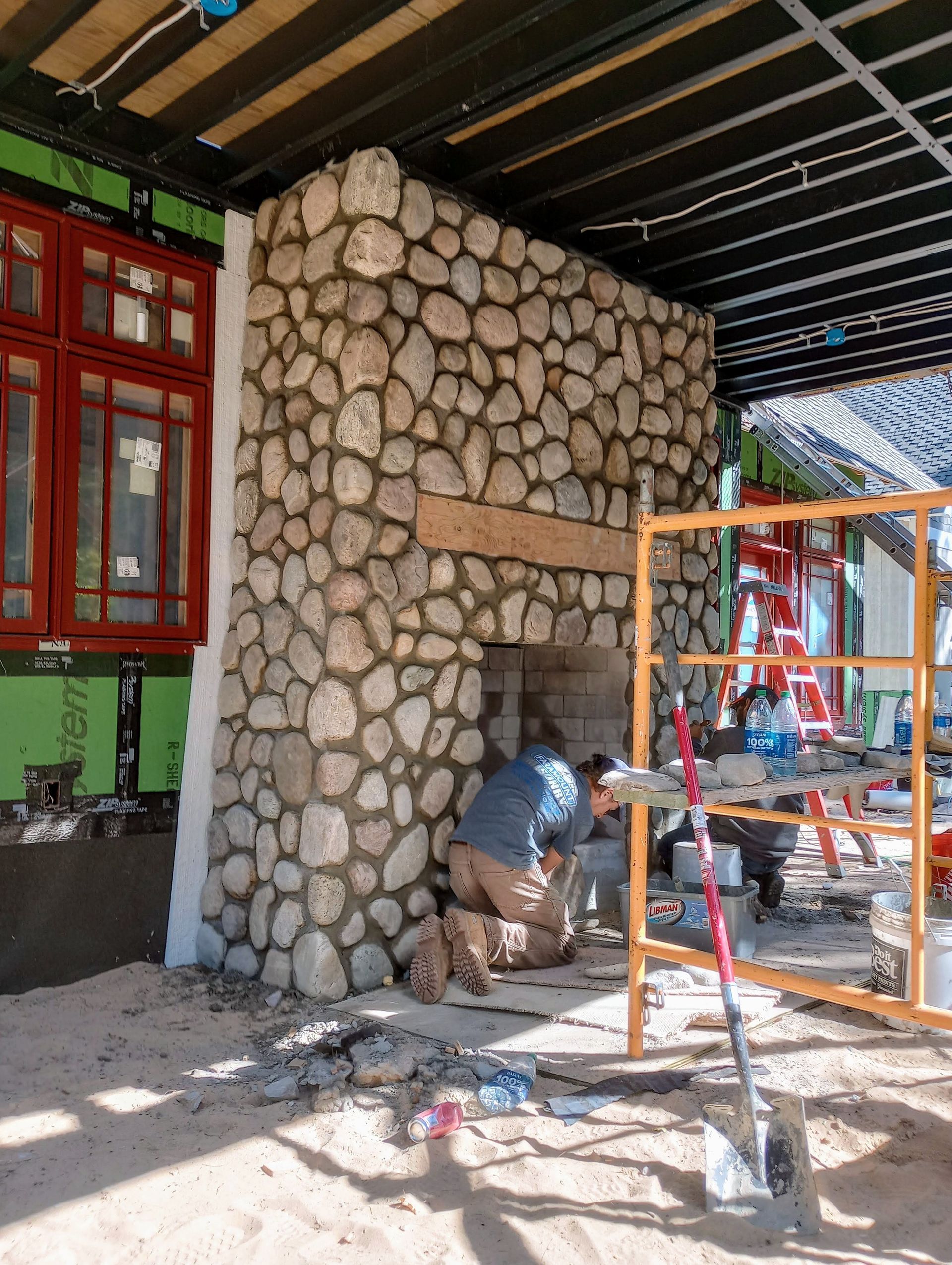 A man is working on a stone fireplace in a house under construction.