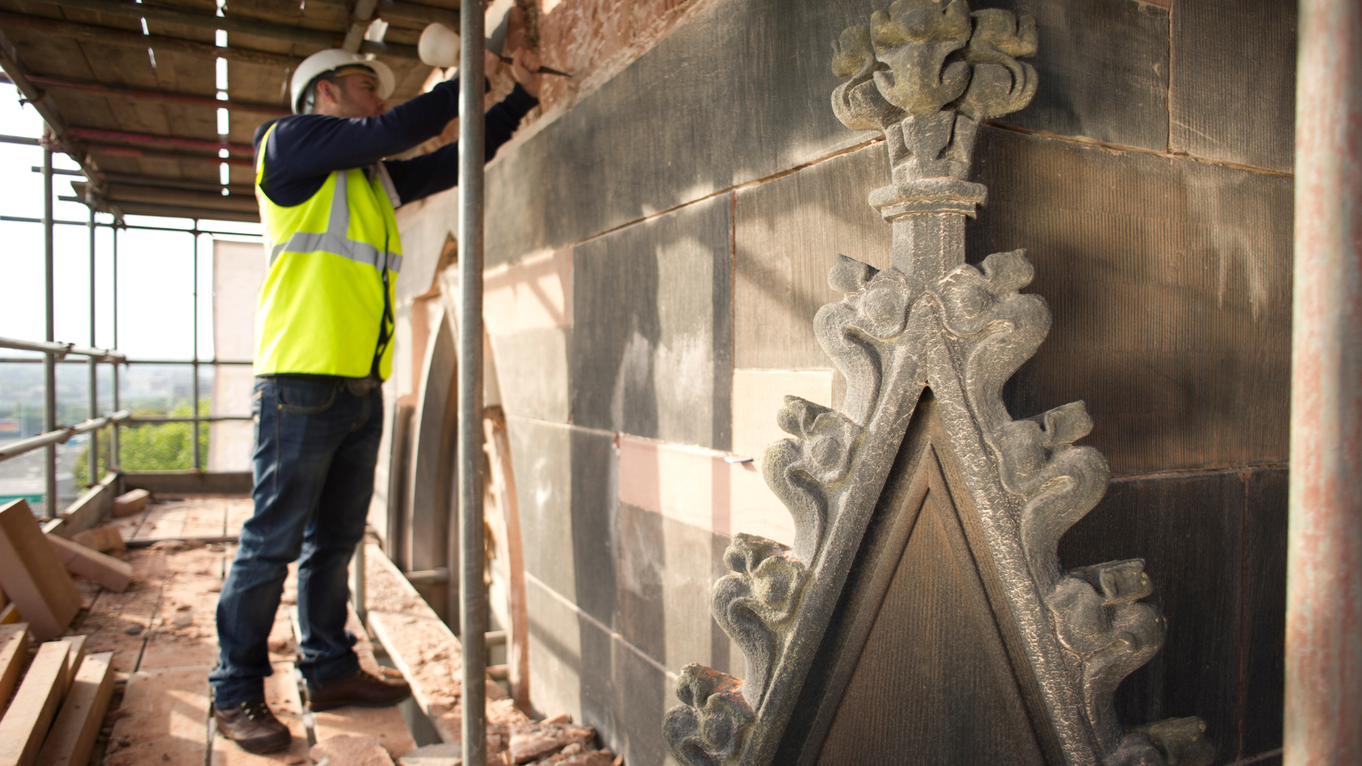 A man in a yellow vest and hard hat is working on a building.
