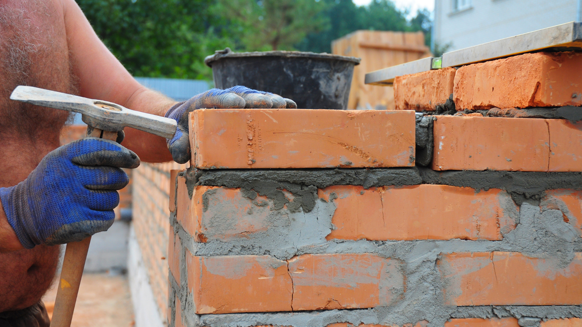 A man is laying bricks on a wall with a hammer.