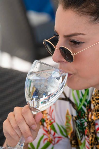 Woman wearing sunglasses sips from a wine glass. She wears a tropical print shirt.