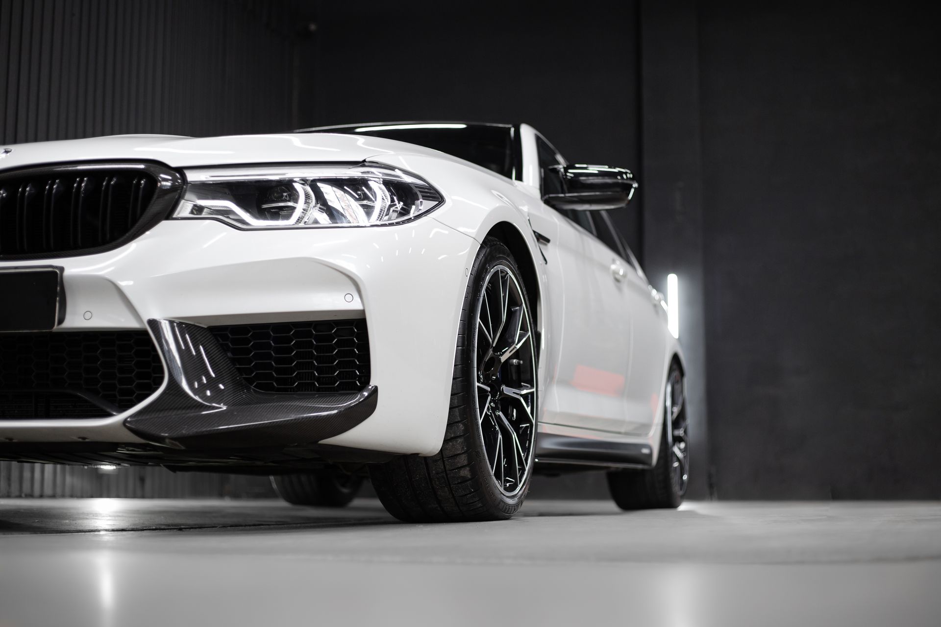 A low-angle view of a white BMW sedan with black rims parked in a dimly lit, modern indoor garage.