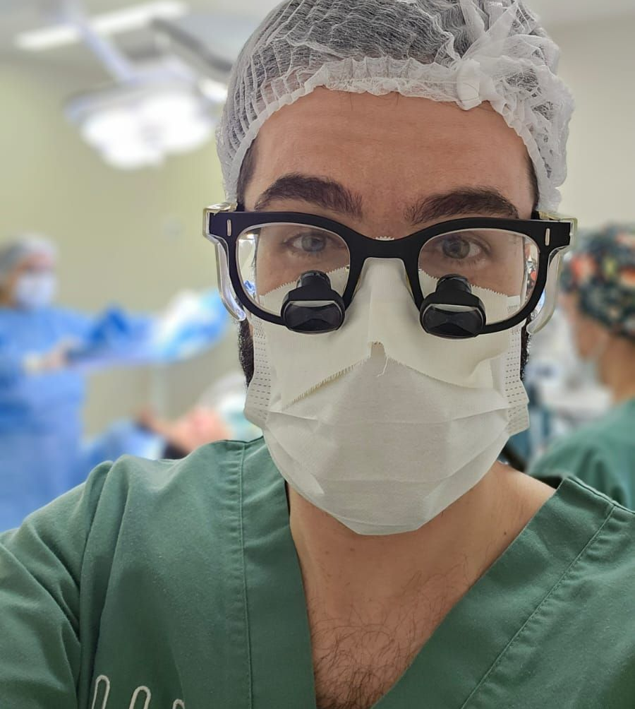 No centro cirúrgico com o Dr. Thomas: técnica microcirúrgica em nervos periféricos, com foco em alívio da dor e recuperação funcional. Dr. Thomas Marcolini no centro cirúrgico, paramentado com gorro, máscara e óculos, durante procedimento de nervos periféricos.