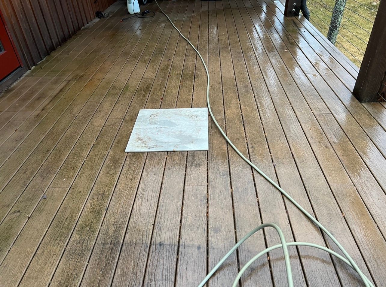 A person is cleaning a wooden deck with a hose.