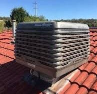 Large, gray evaporative cooler on a red-tiled roof under a blue sky.
