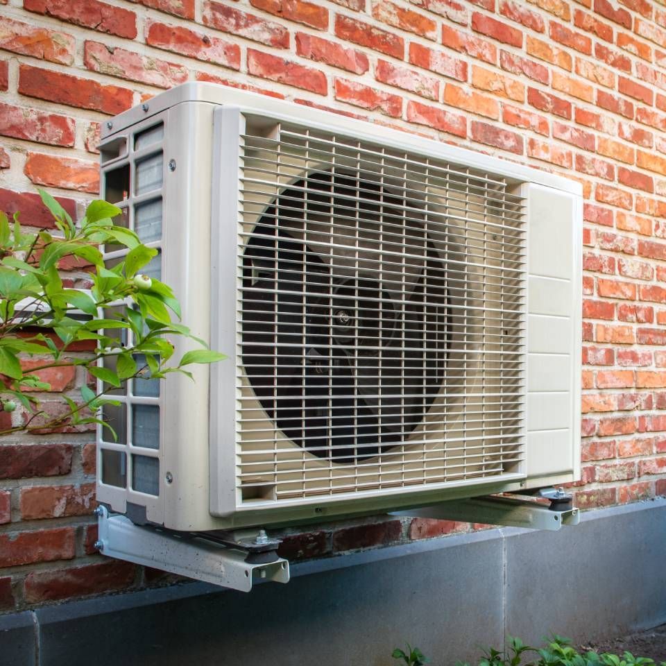 Air conditioning unit mounted on a brick wall, beige with a protective grill.