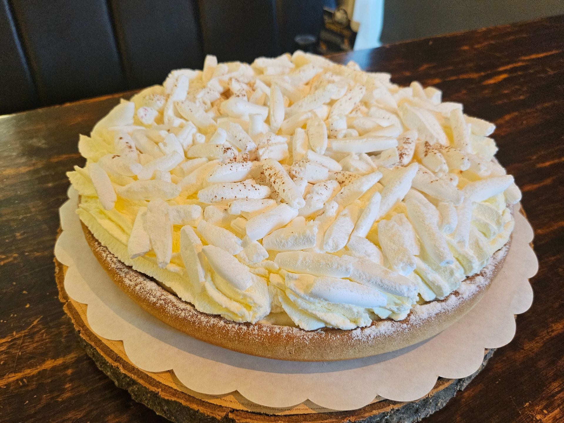 Een ronde vruchtentaart, bedekt met slagroom en witte chocoladeschaafsel.