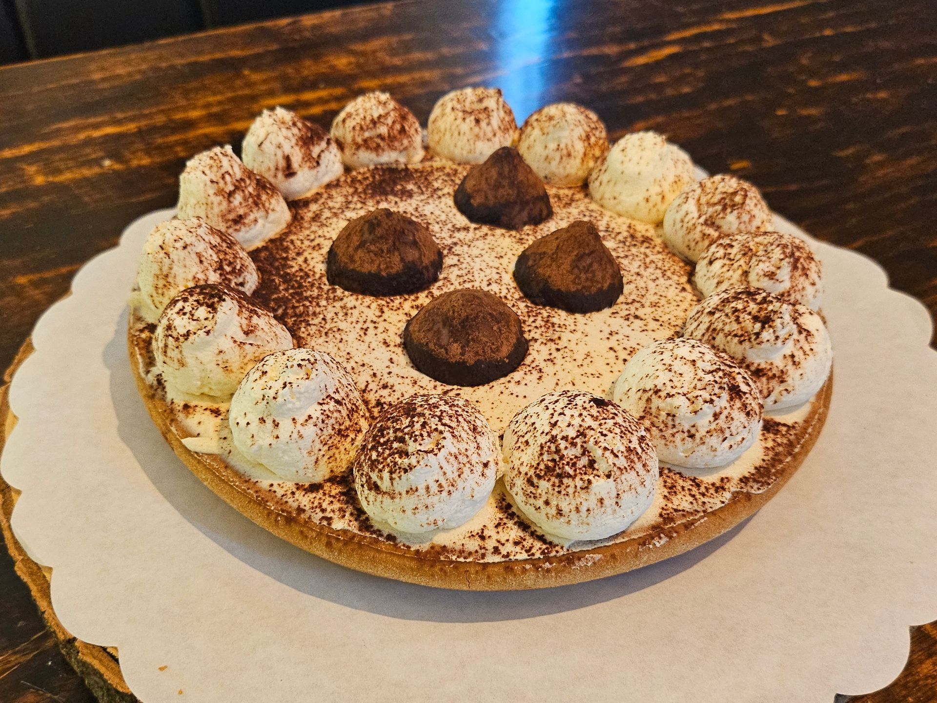 Een ronde taart, bedekt met slagroom, cacaopoeder en vier pure chocoladetruffels.