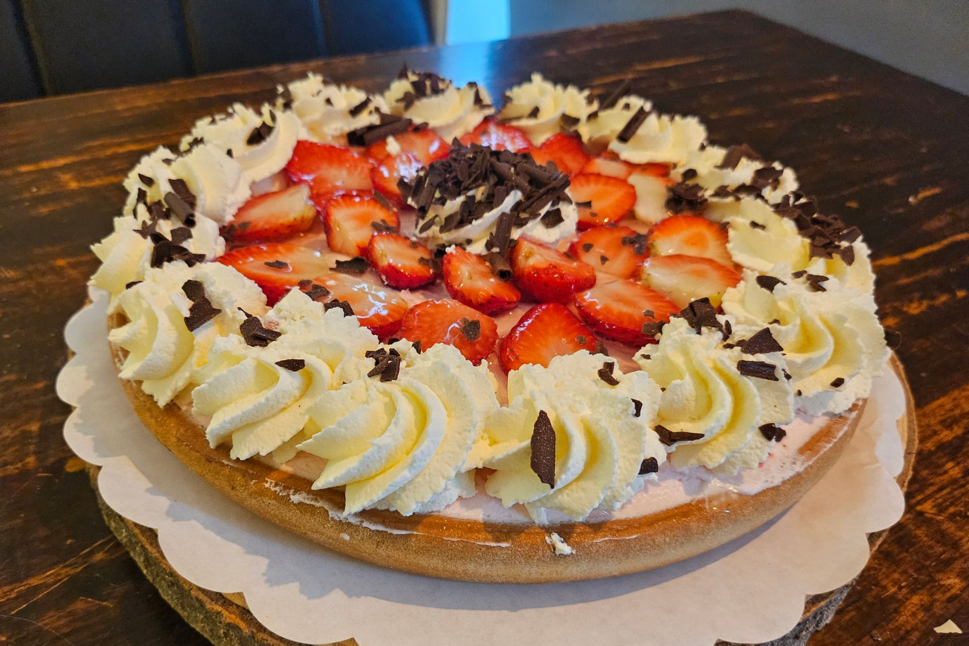 Een ronde aardbeientaart, bedekt met  schijfjes aardbeien, slagroomkrullen en chocoladeschaafsel.