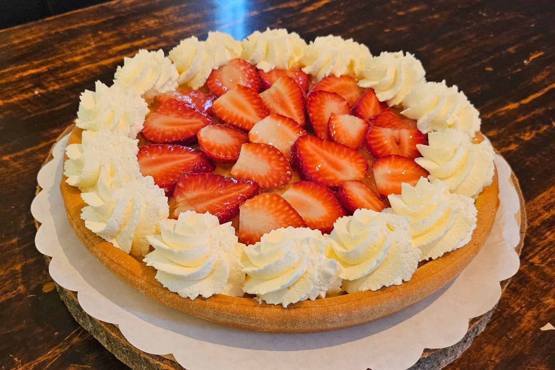 Een ronde aardbeientaart, gegarneerd met verse plakjes aardbeien en een decoratieve rand van slagroom.