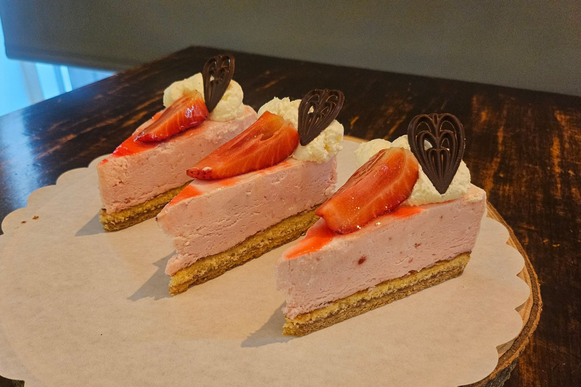 Drie plakjes aardbeiencheesecake, gegarneerd met plakjes aardbei en een hartje.