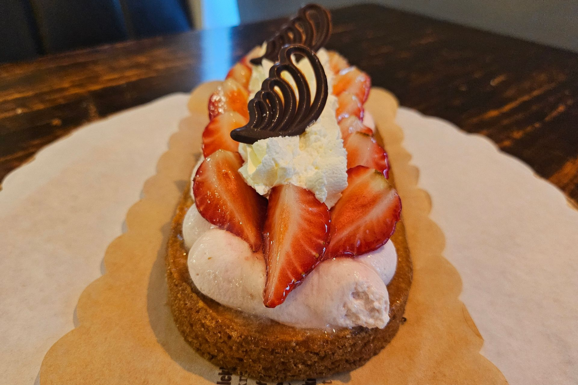 Een aardbeientaartje met slagroom en twee decoratieve chocoladekrullen.