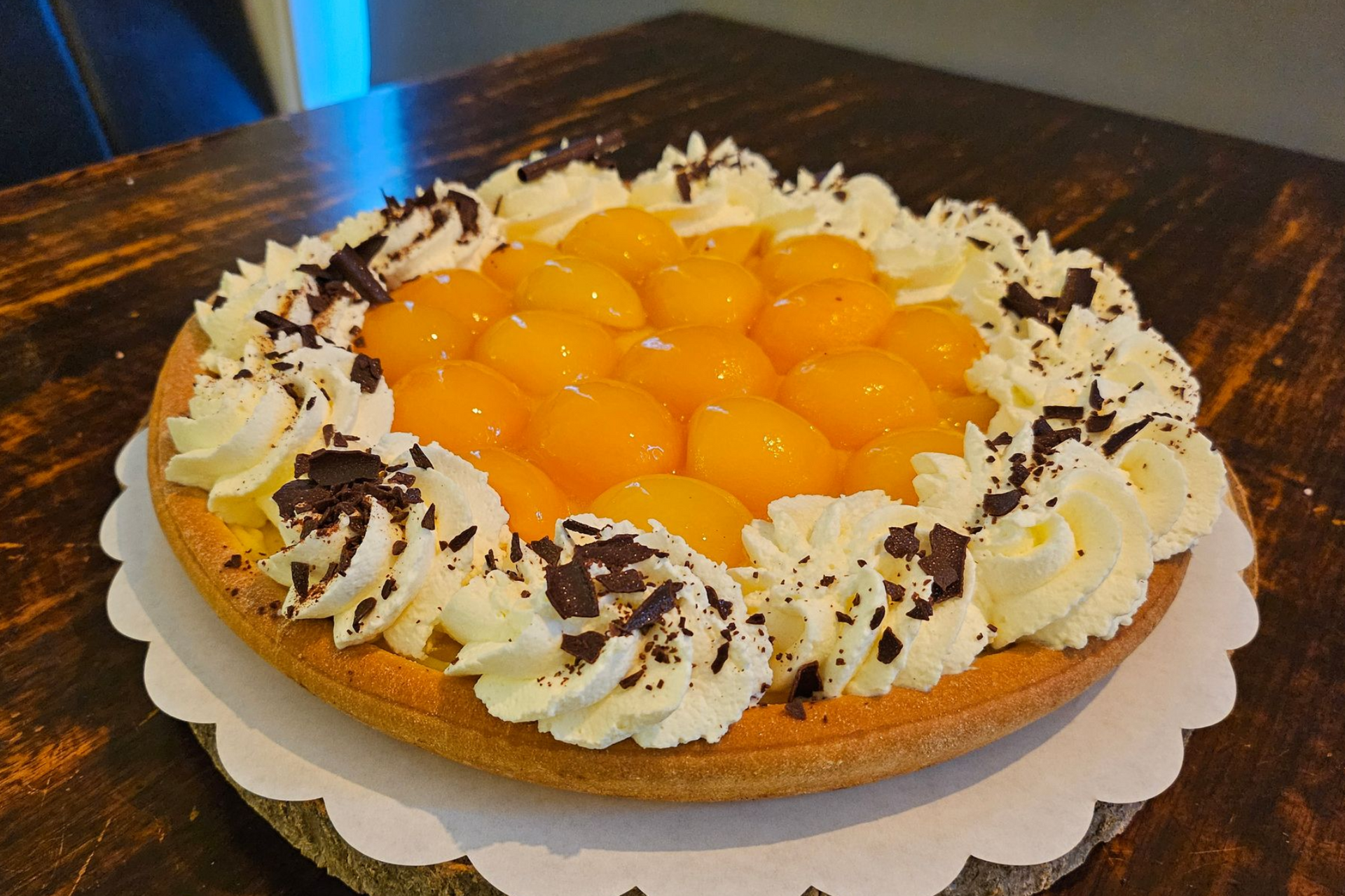 Een fruittaart met perzikhelften, afgewerkt met slagroomkrullen en chocoladeschaafsel.