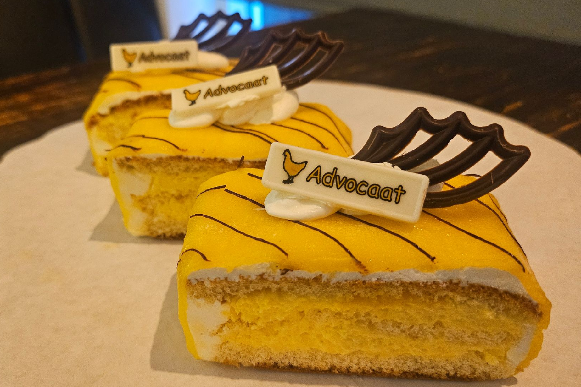 Drie rechthoekige plakken gele Advocaat-cake, versierd met witte chocoladeplakjes en pure chocoladegarnituur.