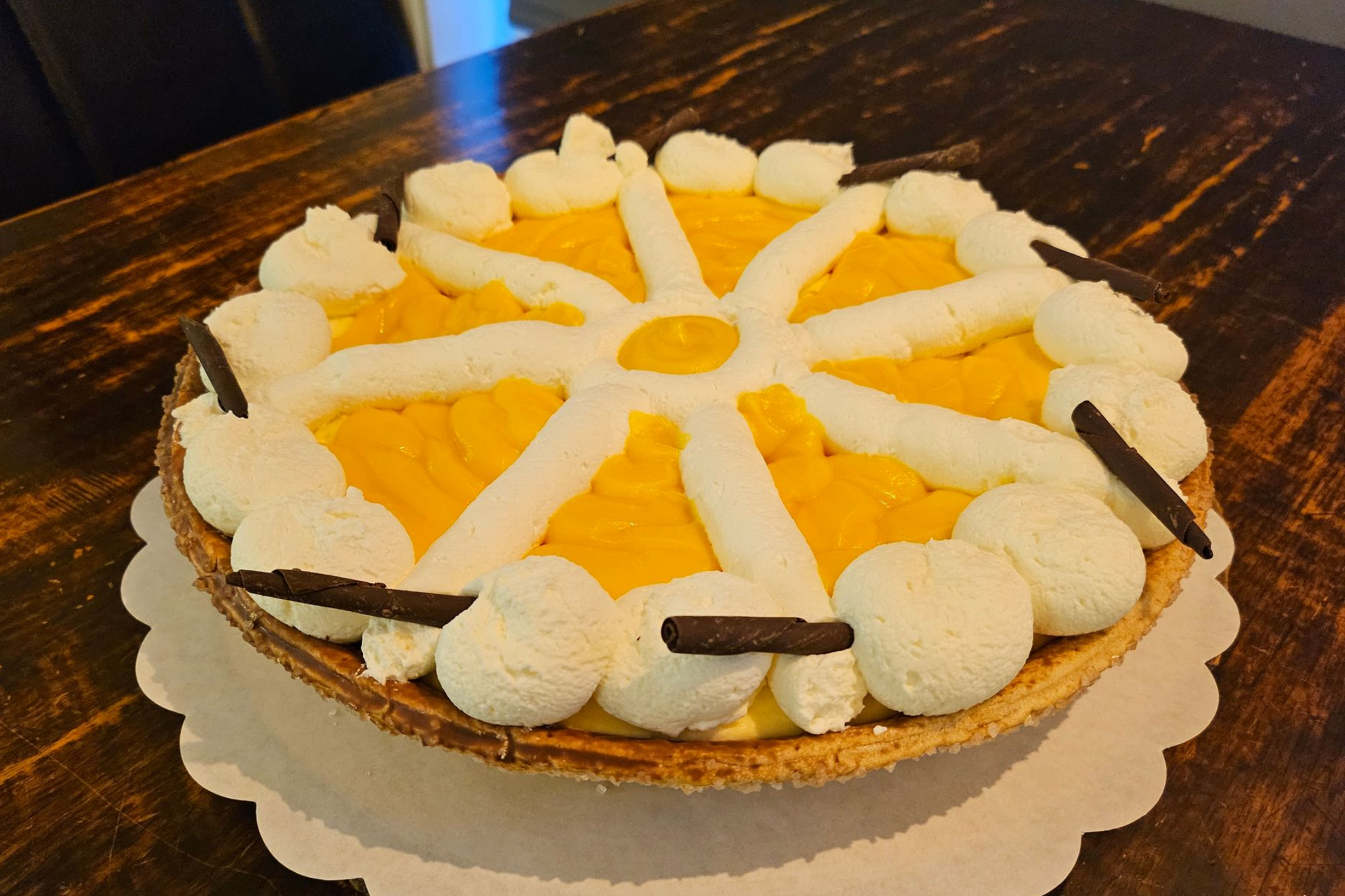 Een ronde advocaattaart met gele vulling, versierd met slagroomsliertjes en kleine chocoladestaafjes.