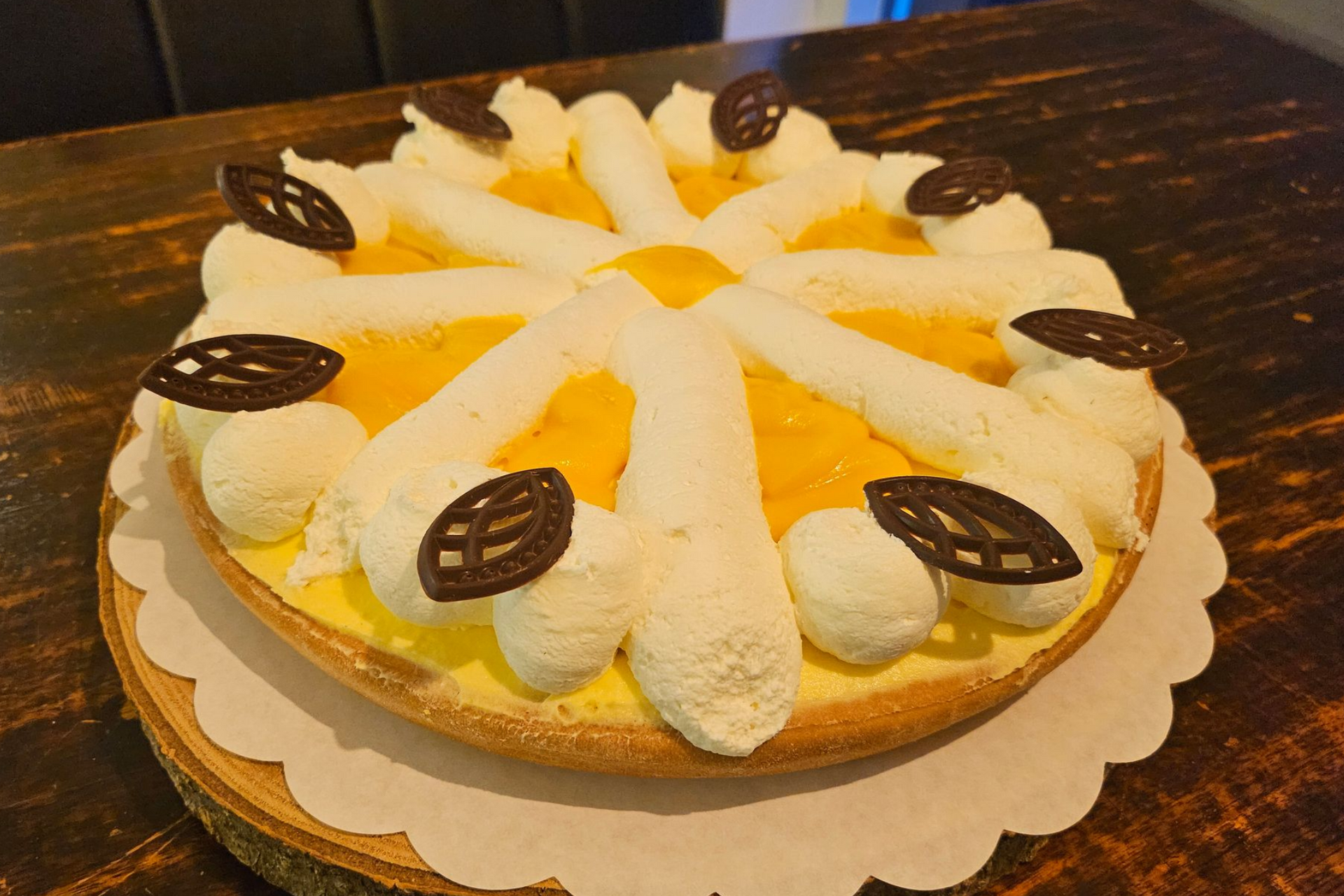 Een ronde vruchtentaart met gele vulling, afgewerkt met slagroom en kleine chocoladeblaadjes als decoratie.