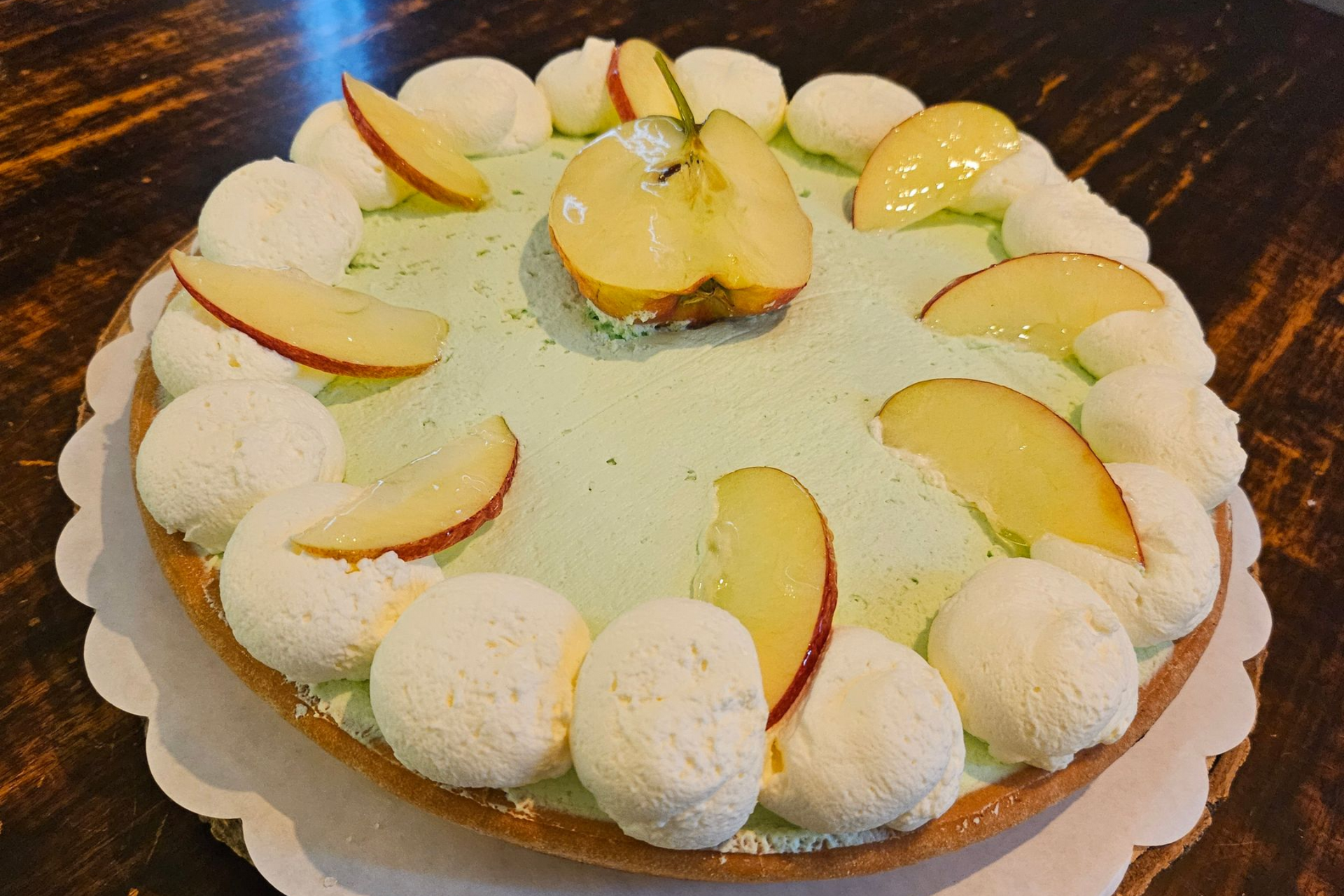 Een ronde taart met lichtgroene vulling, afgewerkt met toefjes slagroom en verse appelschijfjes.