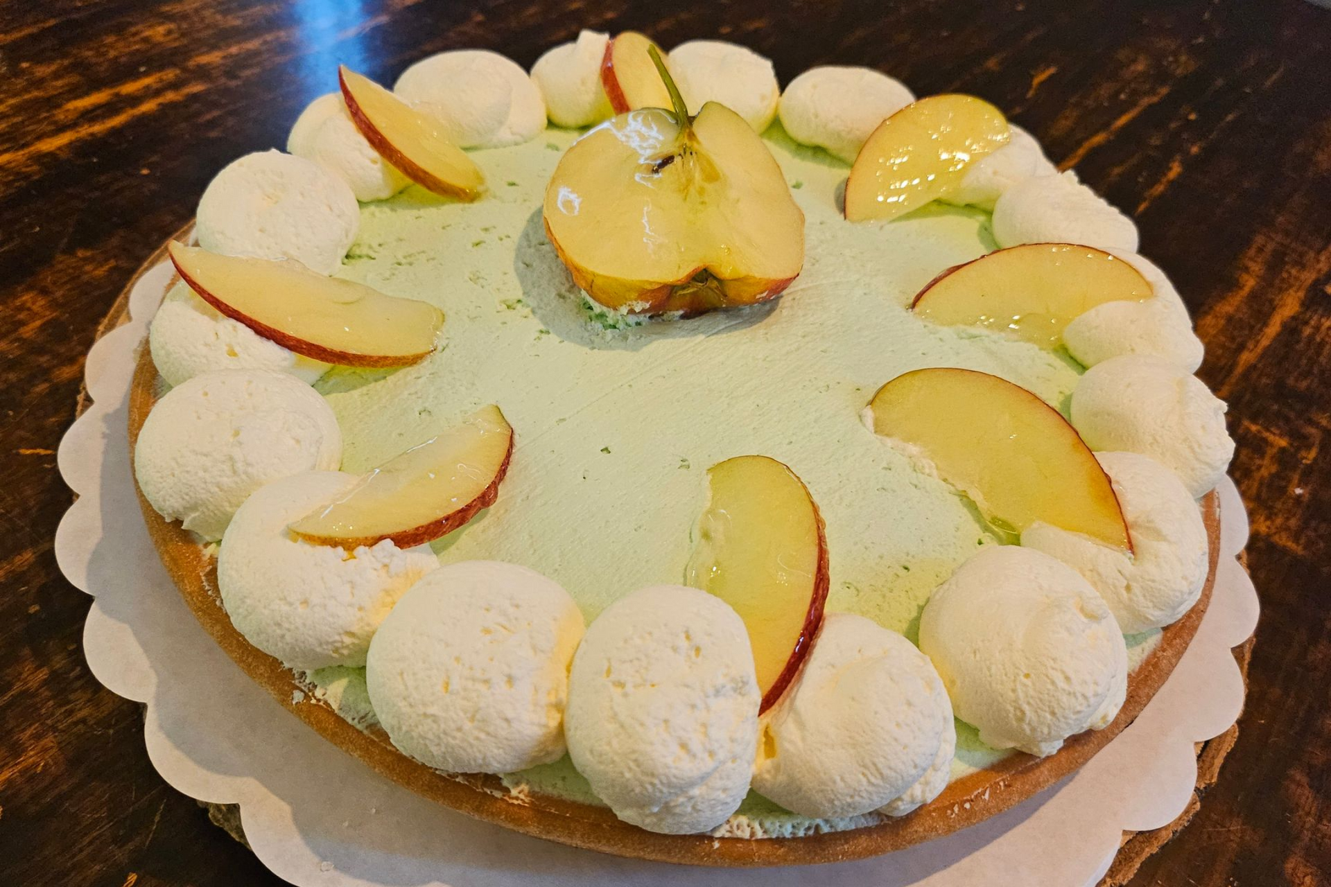 Een lichtgroene desserttaart, versierd met toefjes witte slagroom en verse appelschijfjes.