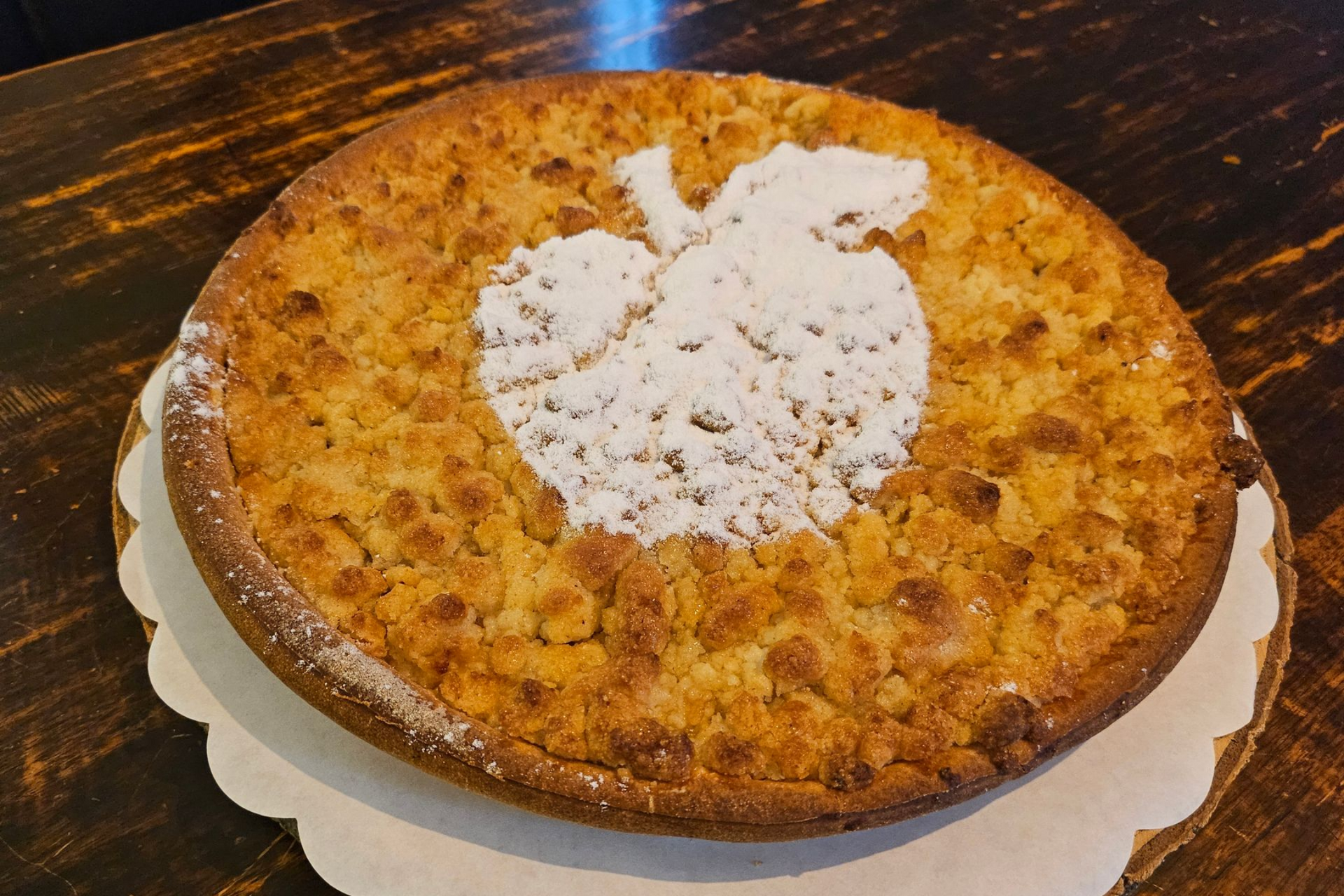 Een goudbruine appelkruimeltaart, met in het midden een appelvormig sjabloon van poedersuiker.